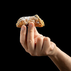 Hand holding Sicilian cannolo on black background. Concept of italian food, dessert, or pastry