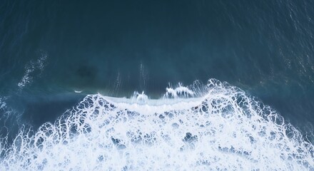 Aerial view of the ocean waves crashing on the shore with white foam and blue water creating a beautiful natural pattern