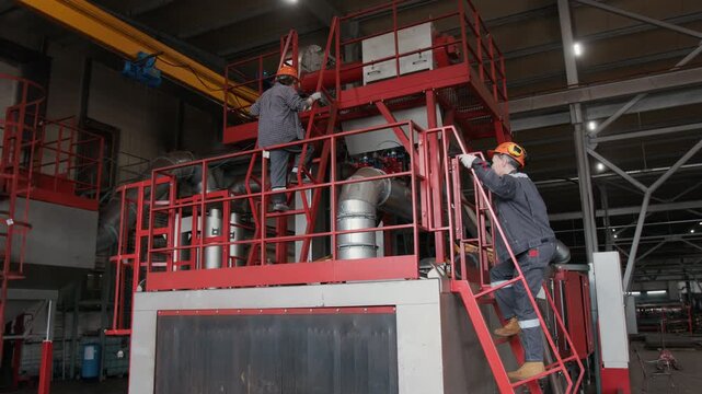 Wide angle shot of middle aged female supervisor and young technician climbing elevated machine platform to inspect machinery in industrial shop floor