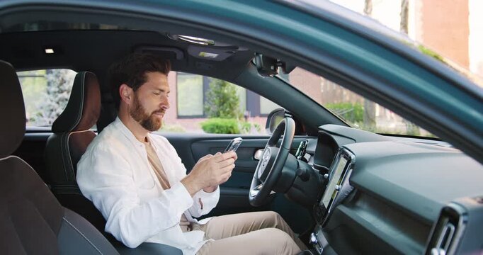 Modern man setting up navigation and music on phone inside stylish vehicle. Concept of technology, travel, connection, and modern lifestyle