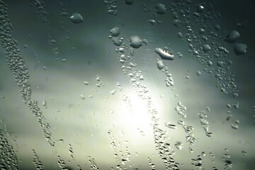 Abstraktes Motiv mit Regentropfenmuster vor grauem bewölktem Himmel mit Sonne bei Regen, Sturm und Sonnenuntergang am Abend im Herbst