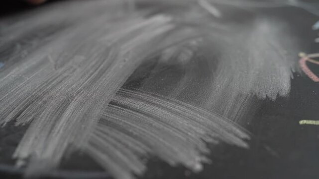 Detailed shot of a hand smudging and erasing a sketch on a dark chalkboard. The educator is preparing the board for a fresh lecture