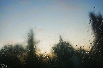Abstraktes Motiv mit Regentropfenmuster auf feuchter Glasscheibe vor Wald und Himmel in der Natur bei Sonnenuntergang, Sturm und Regen am Abend im Herbst