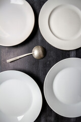 Big white plates and iron spoon on black chalkboard background. Flat lay. Top view. Food concept. Dark mood food photography.