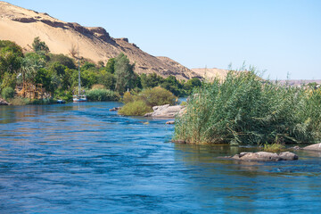 Blue water of river Nile, close to the city of Aswan, Egypt, in the area of native Nubian villages. Desert dune in the background.