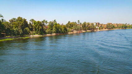 The eastern bank of the river Nile, Egypt, with palm trees and a small village. Blue waters on the foreground. Blue sky on the background. With copy space.