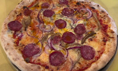 Spicy sausage pizza with red onion and melted cheese on wooden table
