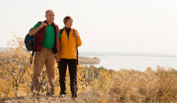 Happy senior couple with backpacks  embracing  Standing on the mountain each other on a warm  autumn day. copy space. 