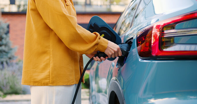 Close-up of female hands connecting an electric car charger to her vehicle outdoors
