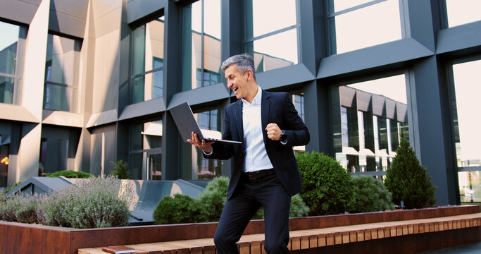 Handsome older man entrepreneur using laptop remotely computer for online business. Focused mature successful businessman working, scrolling, typing on laptop sitting outdoors at office building