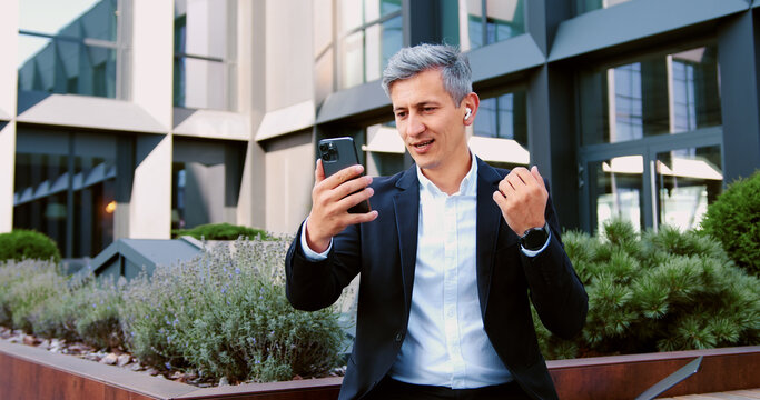Focused mature man sits on a bench near office building having online meeting, Middle aged businessman using laptop while talking on a video call.