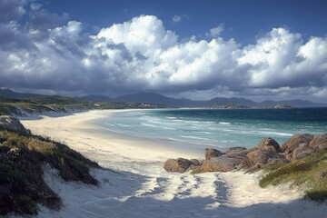 Serene beachscape with white sandy shore, rocky outcrops, gentle ocean waves, distant mountains, and dramatic cloudy blue sky conveying peaceful natural beauty