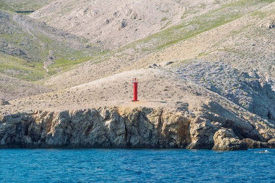Lonely red lighthouse on rocky coastal hills with blue sea