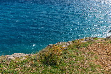 Rocky coastline and vibrant blue ocean waves under clear sky