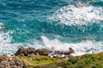 Turquoise waves crashing on rocky seashore with lush greenery