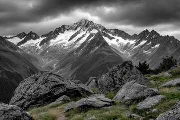 Obraz premium Rugged snow-capped mountain range under dramatic stormy clouds with rocky foreground.