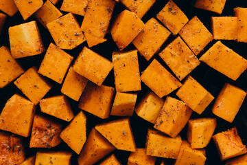 Pumpkin cubes in spices on the tray, prepared to bake, top view.