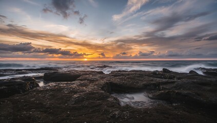 Obraz premium Extended exposure photo capturing a striking coastal scene with rocky shore and vibrant sky during dusk or dawn over the water