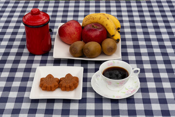 Top view of a coffee cup and a plate with two maple leaf-shaped Wagashi pastries on a navy blue and white plaid tablecloth. Ideal for autumn snack and Japanese food concept.