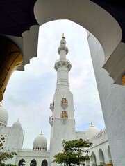 Beautiful mosque minaret framed by a traditional Islamic arch with white marble and golden accents. A serene architectural composition symbolizing peace and spiritual elegance.