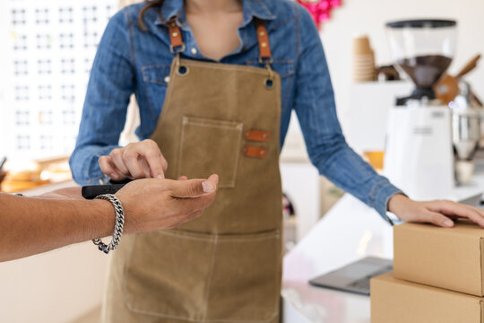 Courier and female small business entrepreneur verifying package via mobile device inside coffee shop, representing modern cashless payment, delivery service reliability, collaboration online orders
