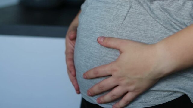 Close up of a woman holding and stroking her belly, second trimester pregnancy 