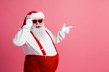 Santa Claus in red suspenders and white coat smiles and points on a pink background for a playful festive Christmas mood