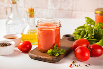 Homemade tomato sauce in glass jar with herbs and tomatoes nearby.
