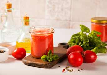 Homemade tomato sauce in glass jar with herbs and tomatoes nearby.