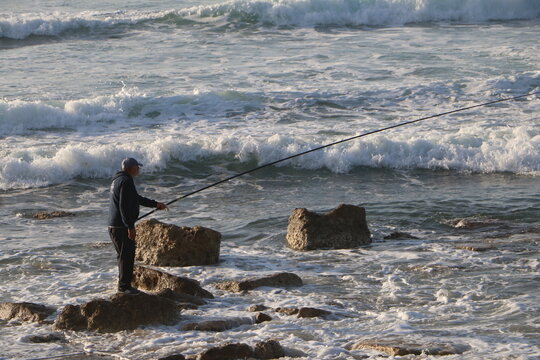 Man fishing on the rocky shore of the sea at sunset. Peaceful seascape scene symbolizing patience, solitude, and connection with nature.
