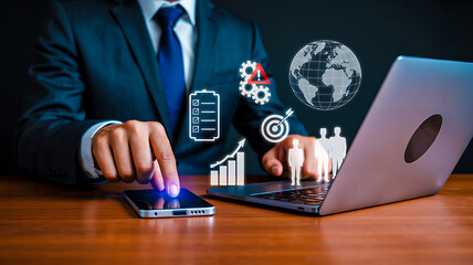 Business professional using smartphone and laptop with digital global data, charts, and business icons in dark office space