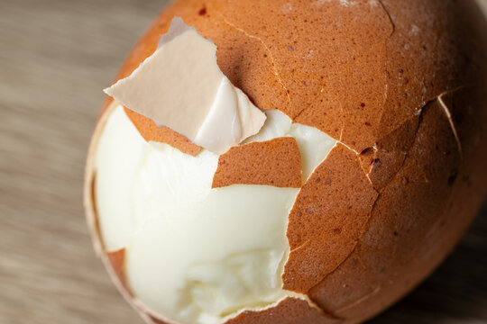 Extreme close up of partially peeled boiled egg with cracked brown shell and creamy texture. Organic breakfast and healthy protein food concept with natural light.