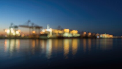 Naklejka premium Blurred night view of a cargo port, showcasing loading and unloading operations, ideal for editorial header background