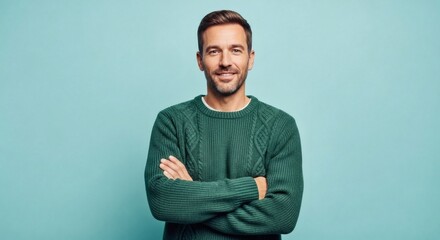 Smiling man with arms crossed wearing a green sweater on a teal background
