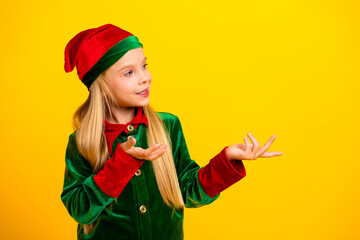 Joyful girl dressed as a Christmas elf presenting with cheerful gestures in front of a vivid yellow background.