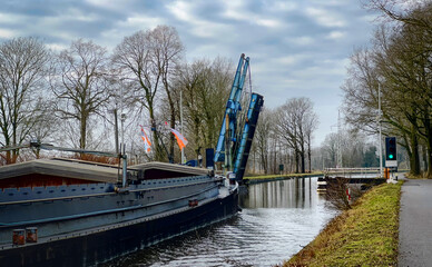 A scenic view features a charming canal boat with a crane, surrounded by lush trees and a calm waterway
