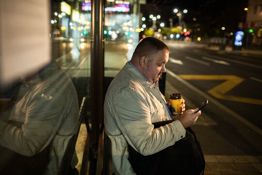 Adult man focused on smartphone at night bus stop