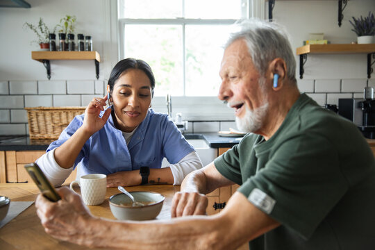 Senior man and adult caregiver smiling on video call in home kitchen