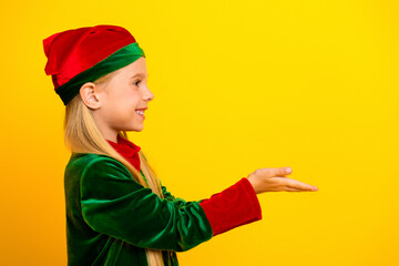 Smiling child in a festive elf costume poses against a vibrant yellow background, ready to spread Christmas cheer and joy