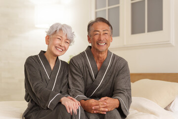 寝室にいるバスローブを着たシニア夫婦（夜）