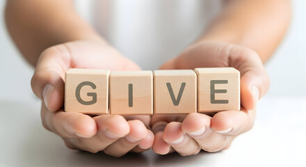 Hands holding wooden blocks spelling the word GIVE, concept of charity.