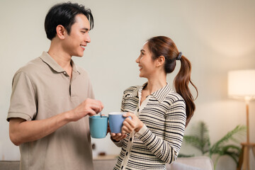 Young Asian couple sharing happy intimate moment at home drinking coffee tea mugs lifestyle daily routine