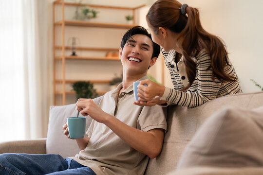 Asian adult couple enjoys morning coffee conversation at home living room relaxed cheerful together intimate bonding moment sharing happy lifestyle wellbeing