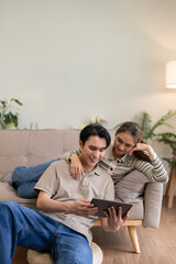 Obraz premium Asian adult couple share digital tablet home living room enjoy online streaming content together happy bonding cozy modern house interior leisure lifestyle moment