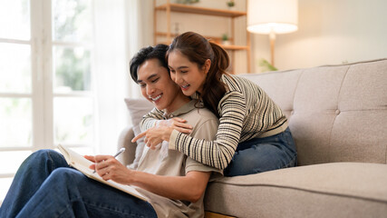 Adult Asian couple planning ideas together at home sharing joyful moments creating future goals in cozy living room