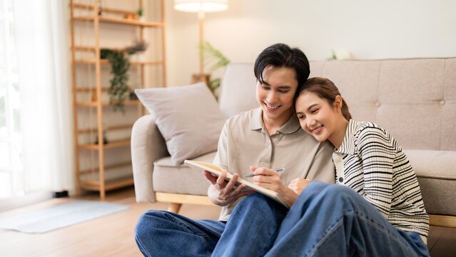 Asian adult couple shares sweet moment writing notes or planning ideas with warmth affection and happy smiles comfortably on living room floor at home - Powered by Adobe