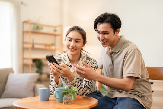 Asian couple sharing smartphone screen browsing content together home environment digital connection modern lifestyle joy happiness domestic comfort