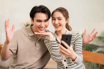 Asian adult couple enjoys digital connection at home smiling cheerfully sharing happy moments online using smartphone for video call or selfie capture