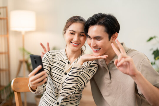 Asian young couple capture selfie phone peace sign smile home social media shared happy moments digital connection