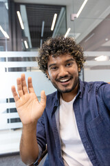 Vertical close-up photo of a young Indian man in an office talking to a camera he is holding in his hand